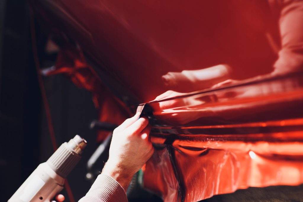 Car wrapping specialist putting vinyl foil or film on car. Selective focus.