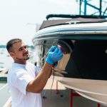 Boat maintenance - Man with orbital polisher polishing boat in marina.