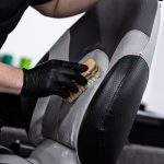 Man car wash worker cleaning leather boat seat with brush and detergent